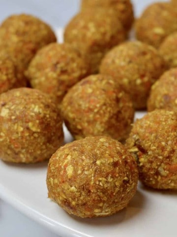 carrot coconut energy balls on a white pedestal with dates and a carrot in the background