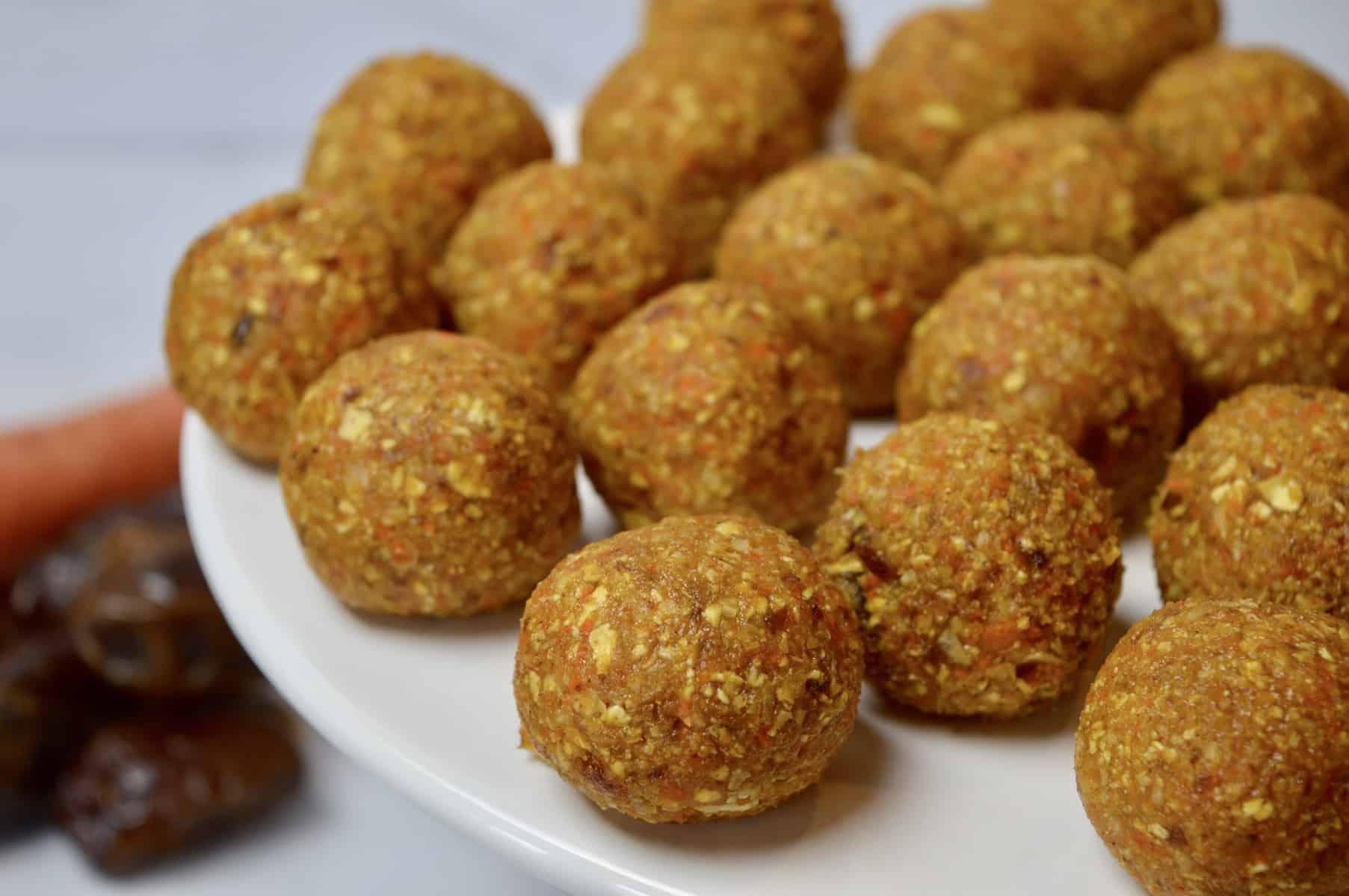 carrot coconut energy balls on a white pedestal with dates and a carrot in the background 