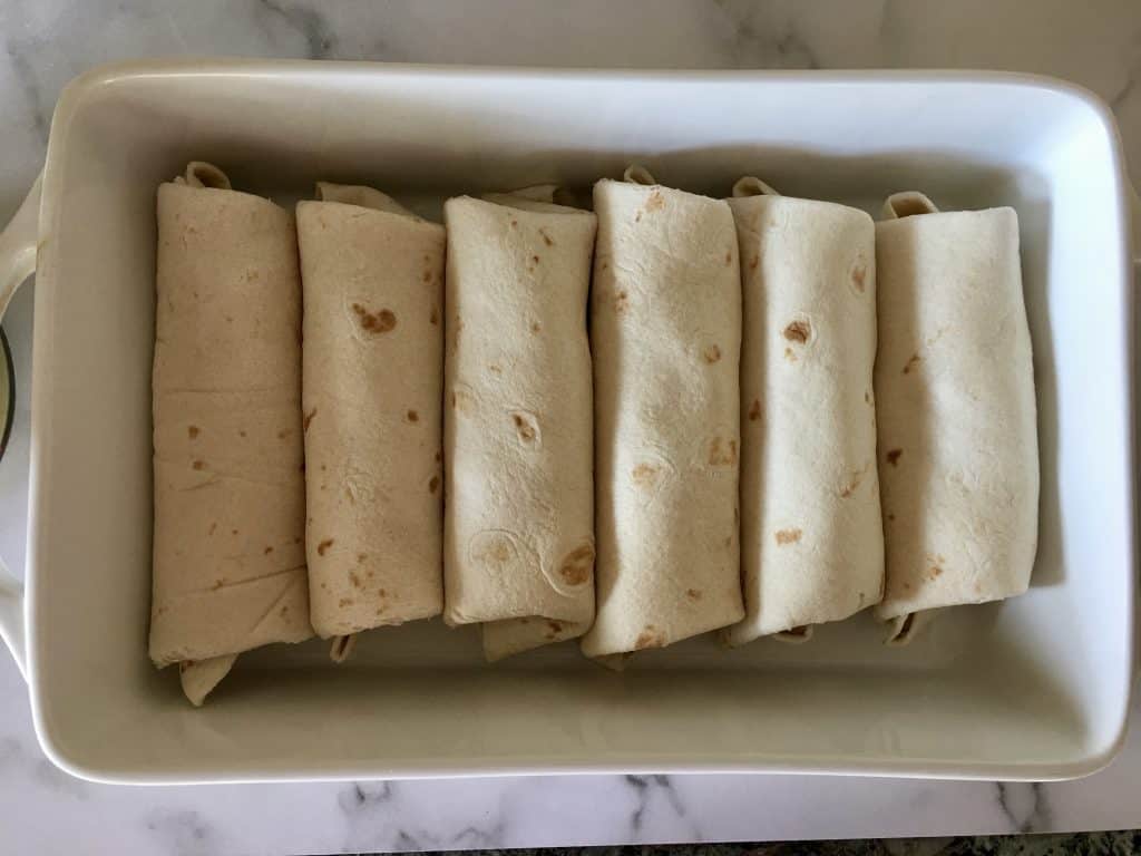 six burritos rolled in a white casserole dish. 