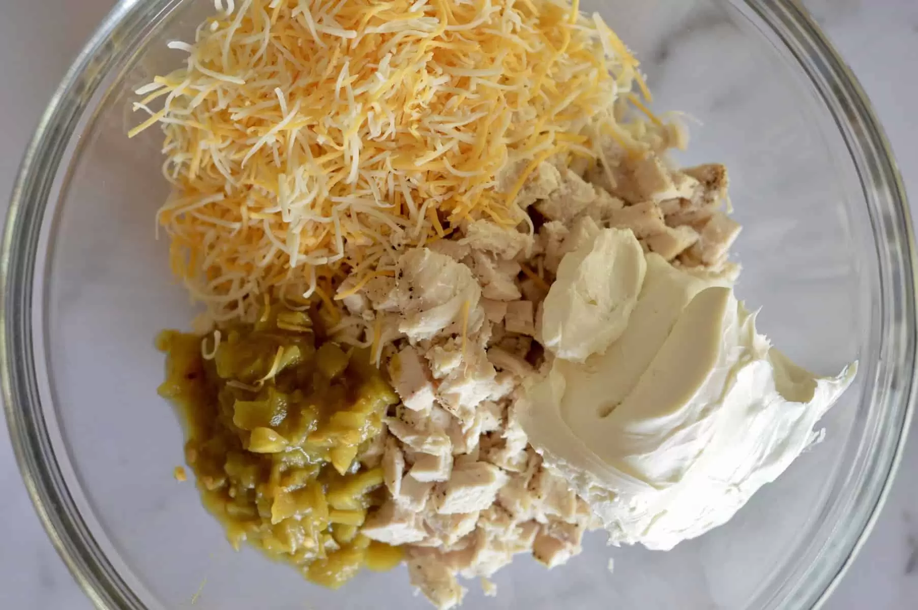 chicken in a bowl along with cream cheese, green chilis, and shredded cheddar cheese.