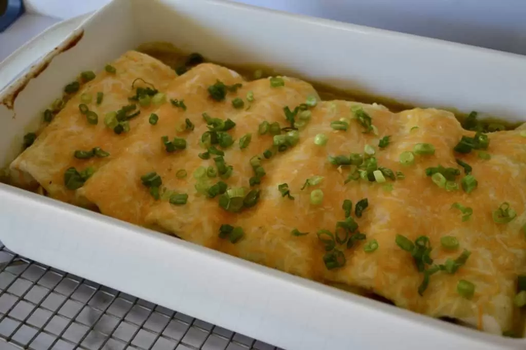 Green Chili Chicken Burritos in a white casserole dish with green onions sprinkled over top. 