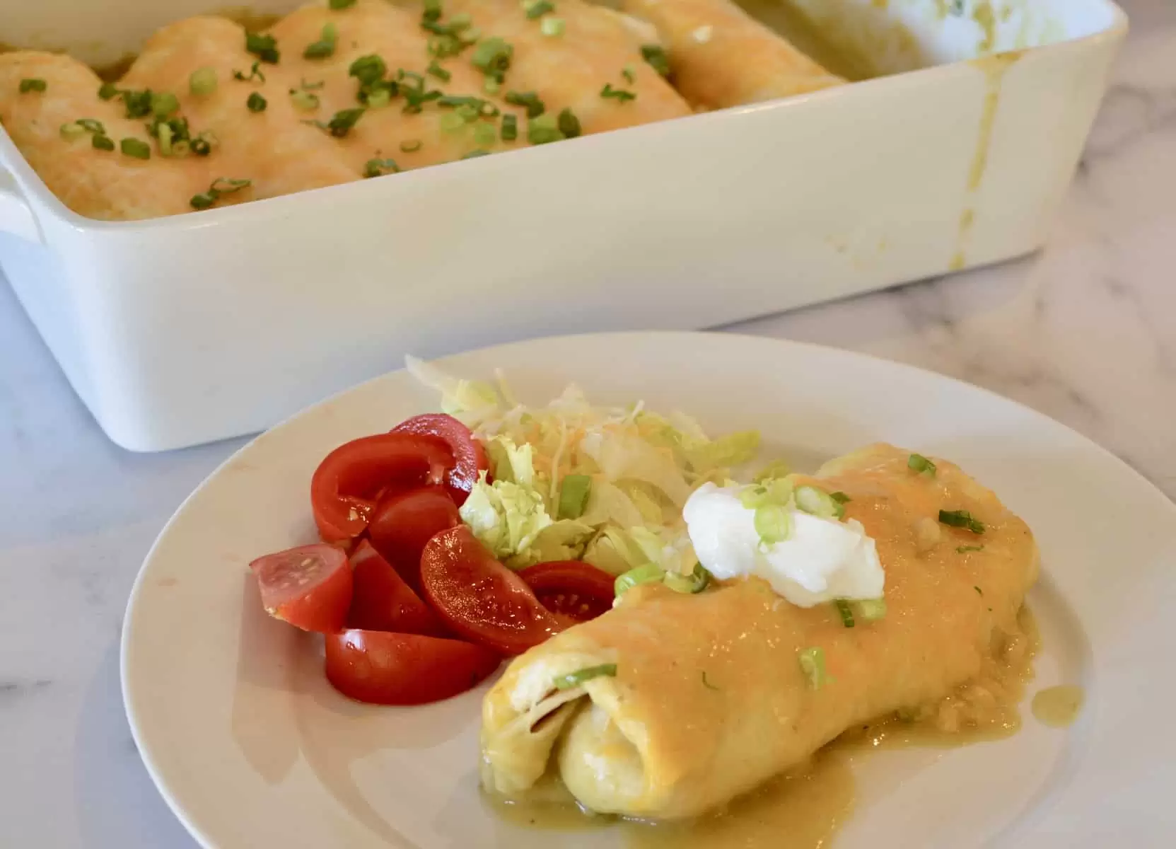 green chili chicken burrito on a white plate with tomatoes and lettuce