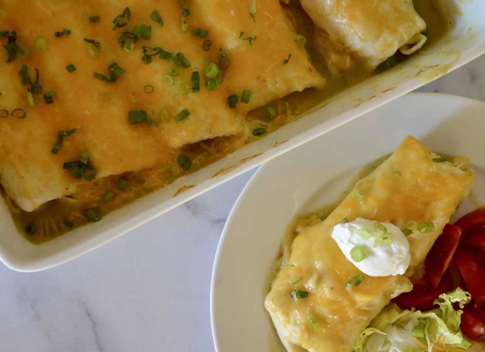 cassorole dish with smothered burritos and a white plate with burrito and tomatoes on it