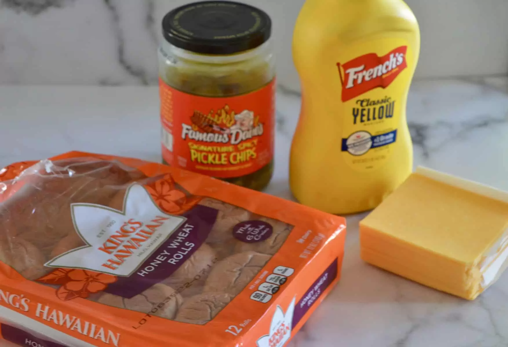 King Hawaiian Buns, pickles, mustard, and cheese on a counter. 