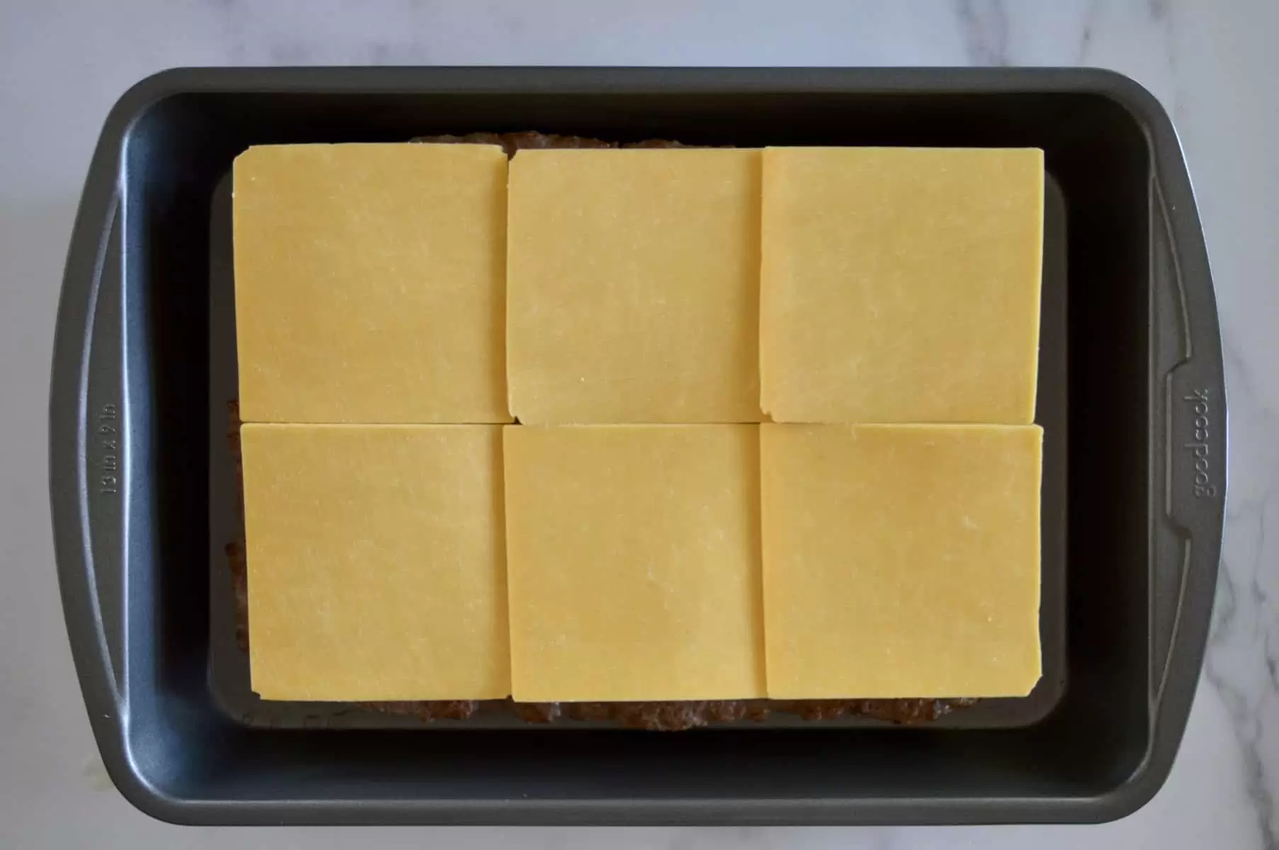 sliced cheese on top of sliders in a baking pan. 