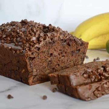 Chocolate Zucchini Banana Bread on a counter with bananas and a zucchini in the background