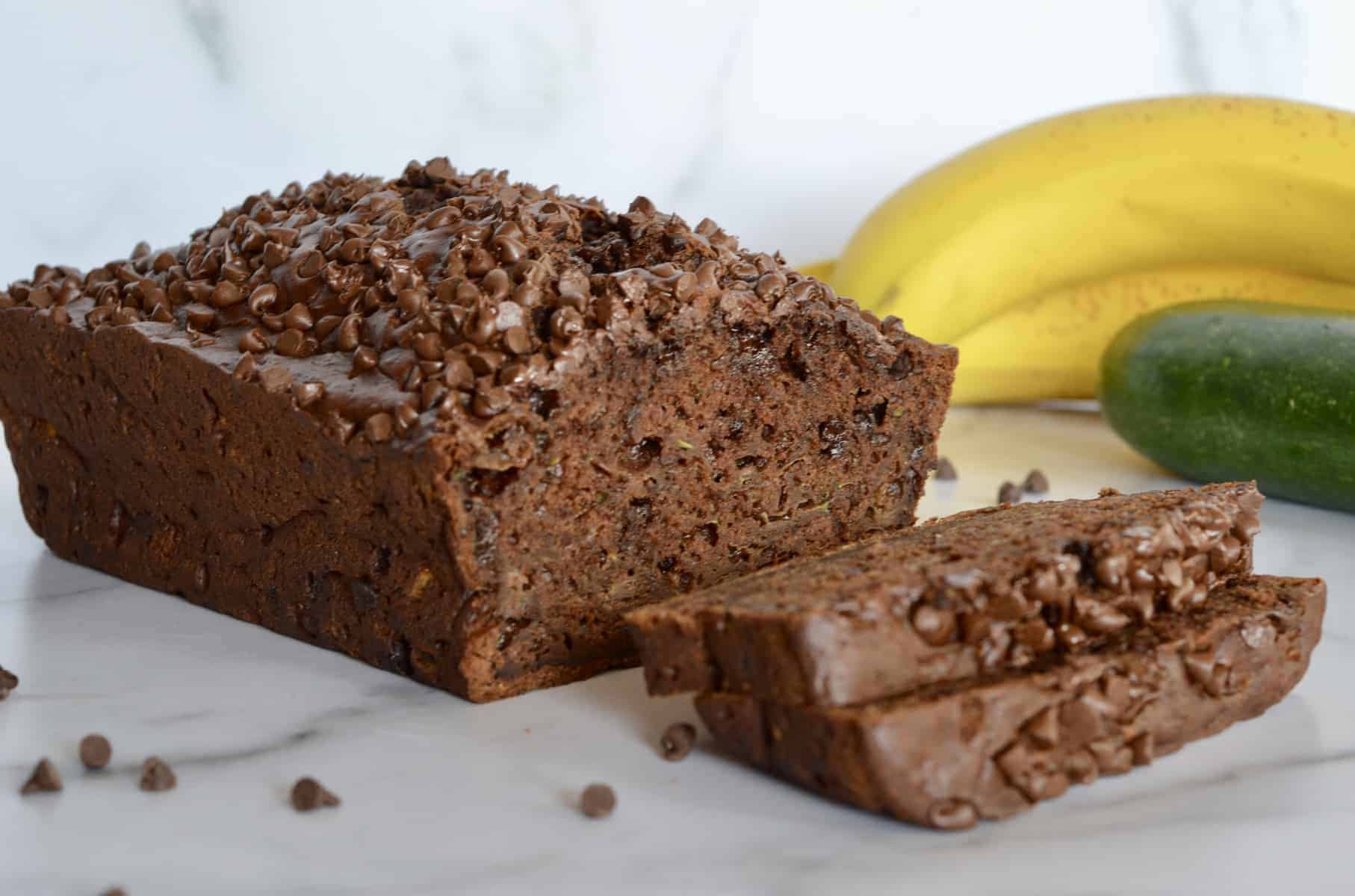 Chocolate Zucchini Banana Bread on a counter with bananas and a zucchini in the background 