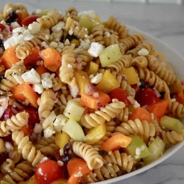 Whole Wheat Greek Pasta Salad with feta, tomatoes, cucumbers, and bell pepper in an white bowl.