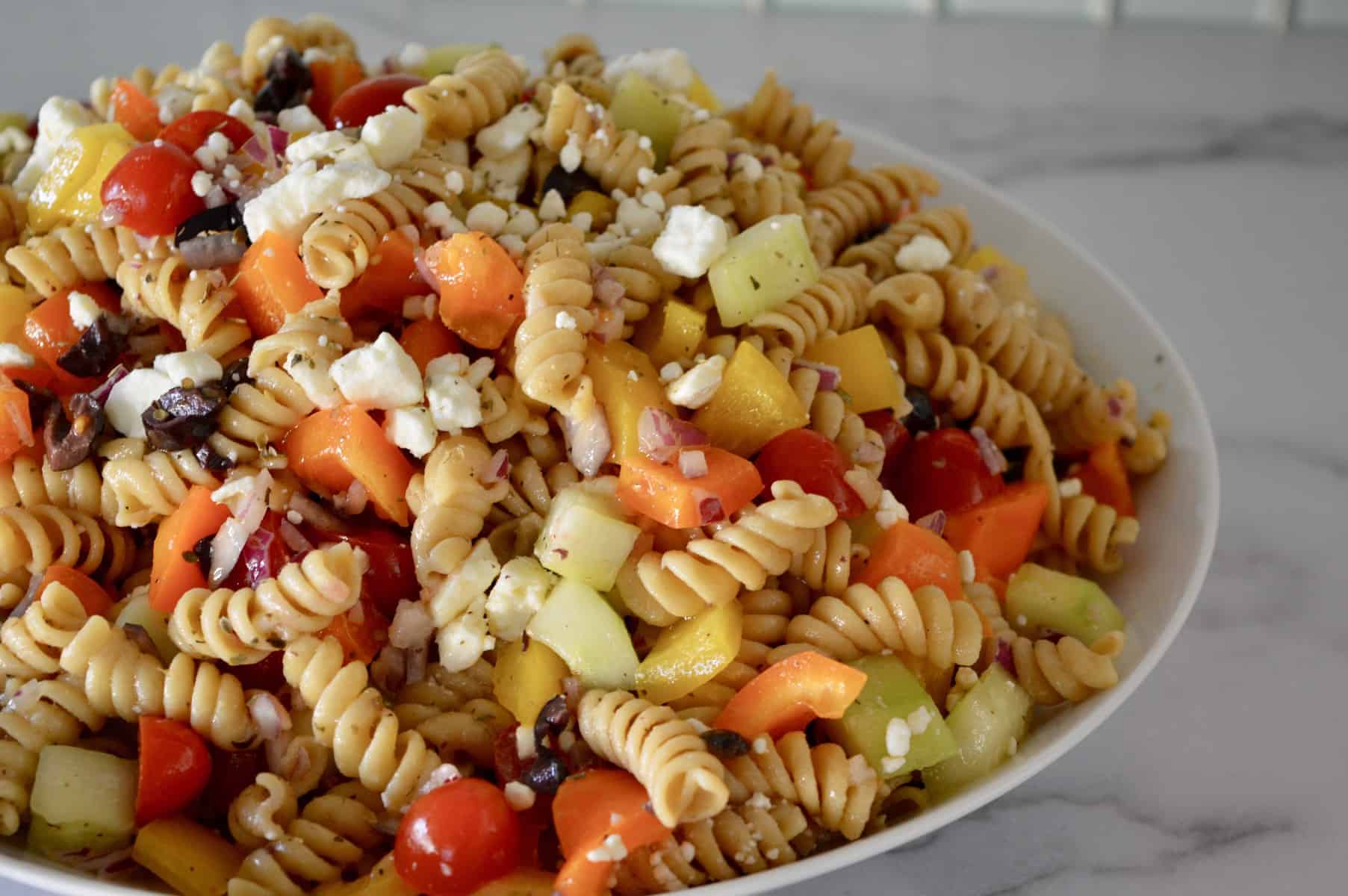 Whole Wheat Greek Pasta Salad with feta, tomatoes, cucumbers, and bell pepper in an white bowl. 