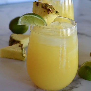 Glass of pineapple margarita with a lime and pineapple garnish.