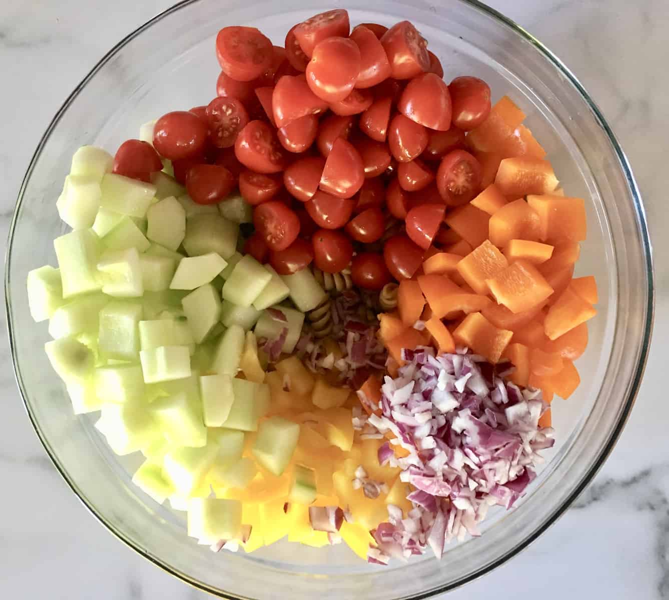 glass bowl full of rotini pasta, bell peppers, cucumbers, tomatoes, and red onions. 