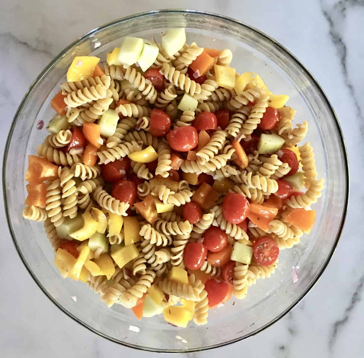 Glass bowl of tossed ingredients and only half of the greek dressing. 