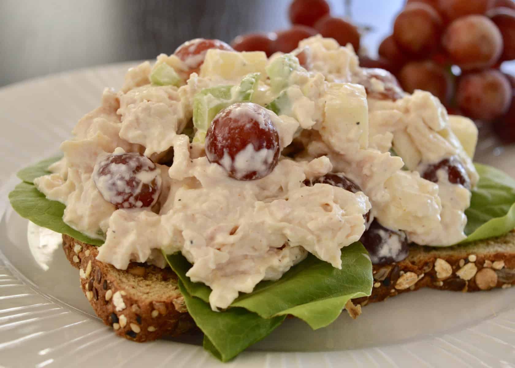Rotisserie Chicken Salad on a piece of whole wheat toast with a side of red grapes. 