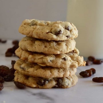 Oatmeal Raisin cookies stacked on a counter with a glass of milk.