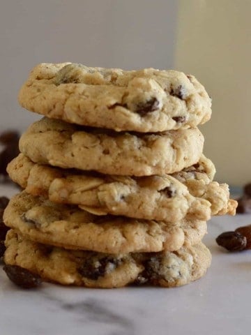 Oatmeal Raisin cookies stacked on a counter with a glass of milk.