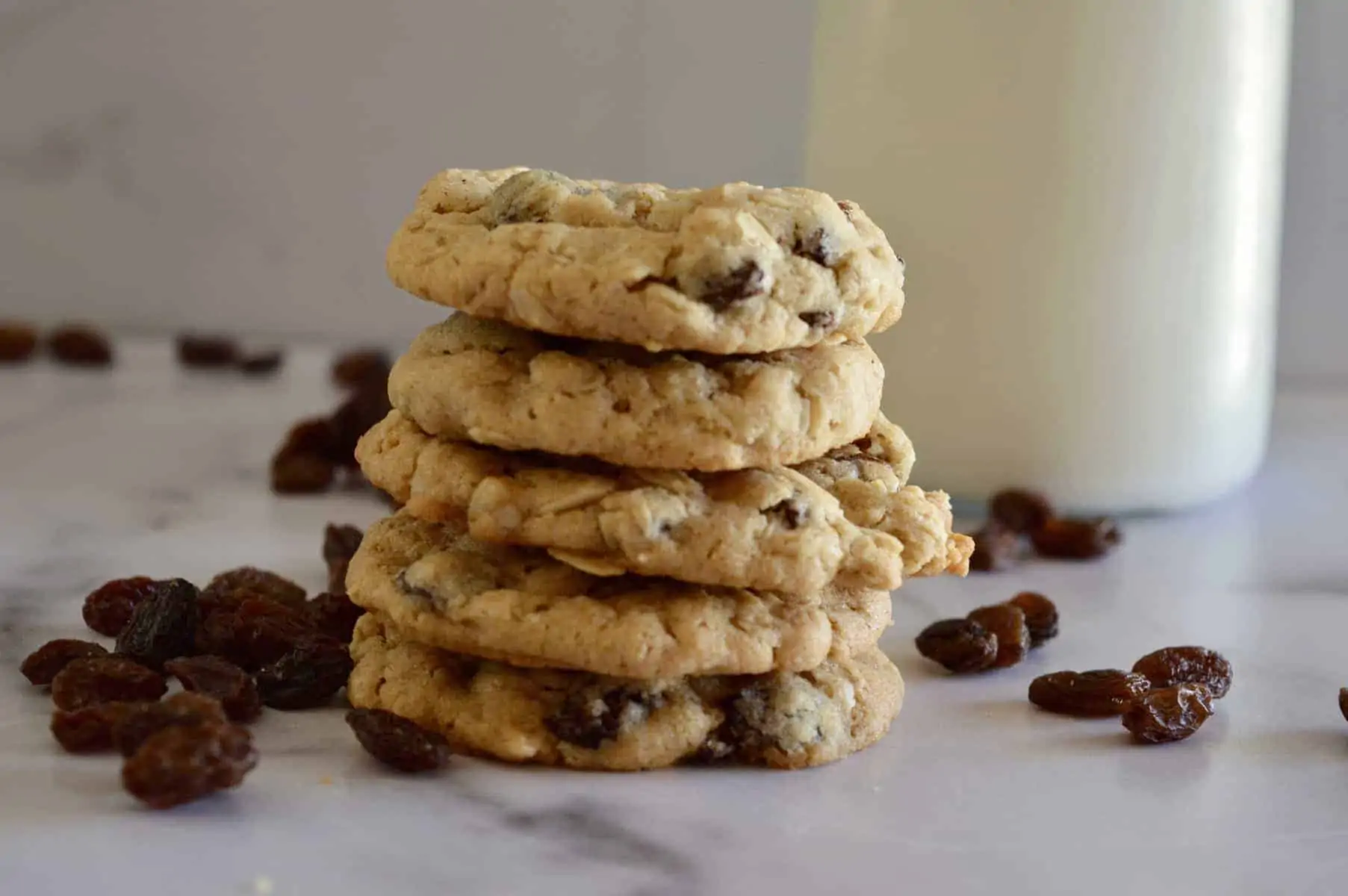 Oatmeal Raisin cookies stacked on a counter with a glass of milk. 
