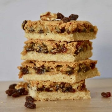 Butter Tart Squares with Walnuts and Raisins stacked on each other on a wooden table.
