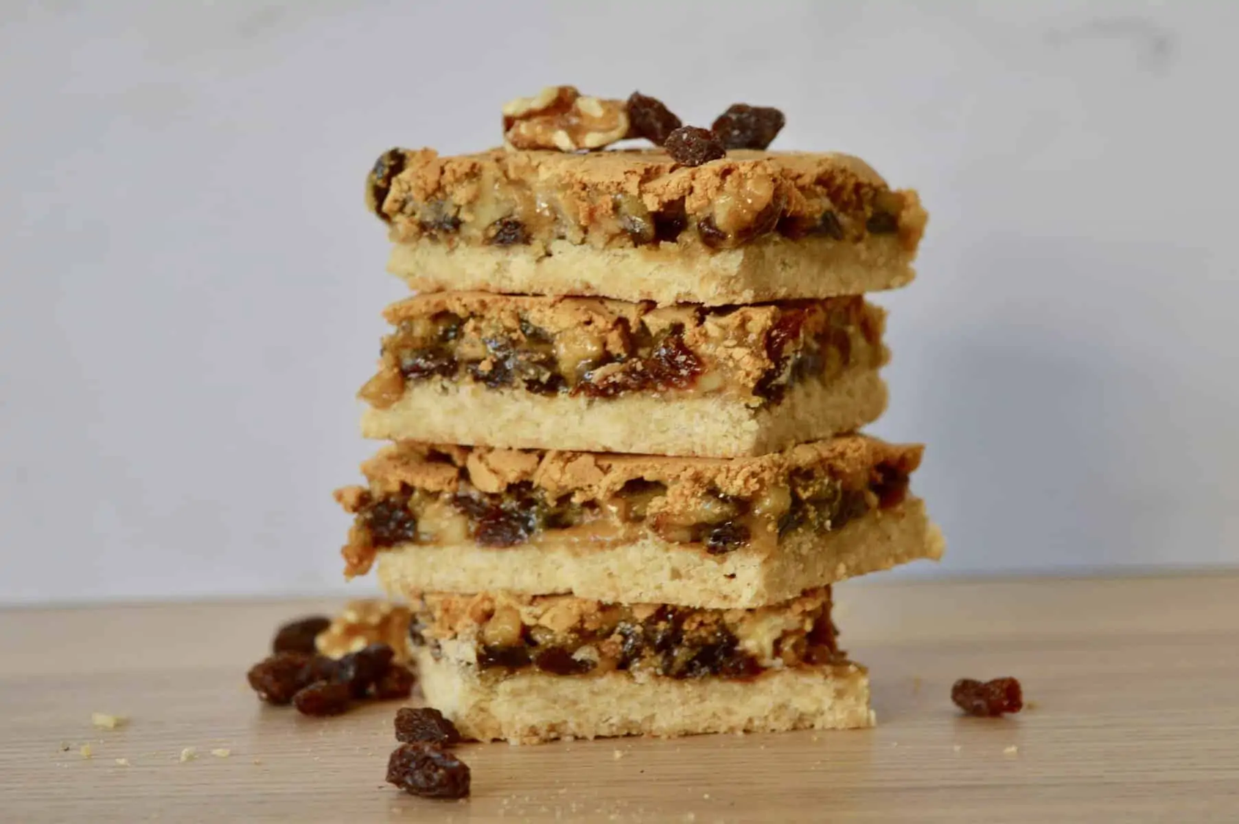 Butter Tart Squares with Walnuts and Raisins stacked on each other on a wooden table. 