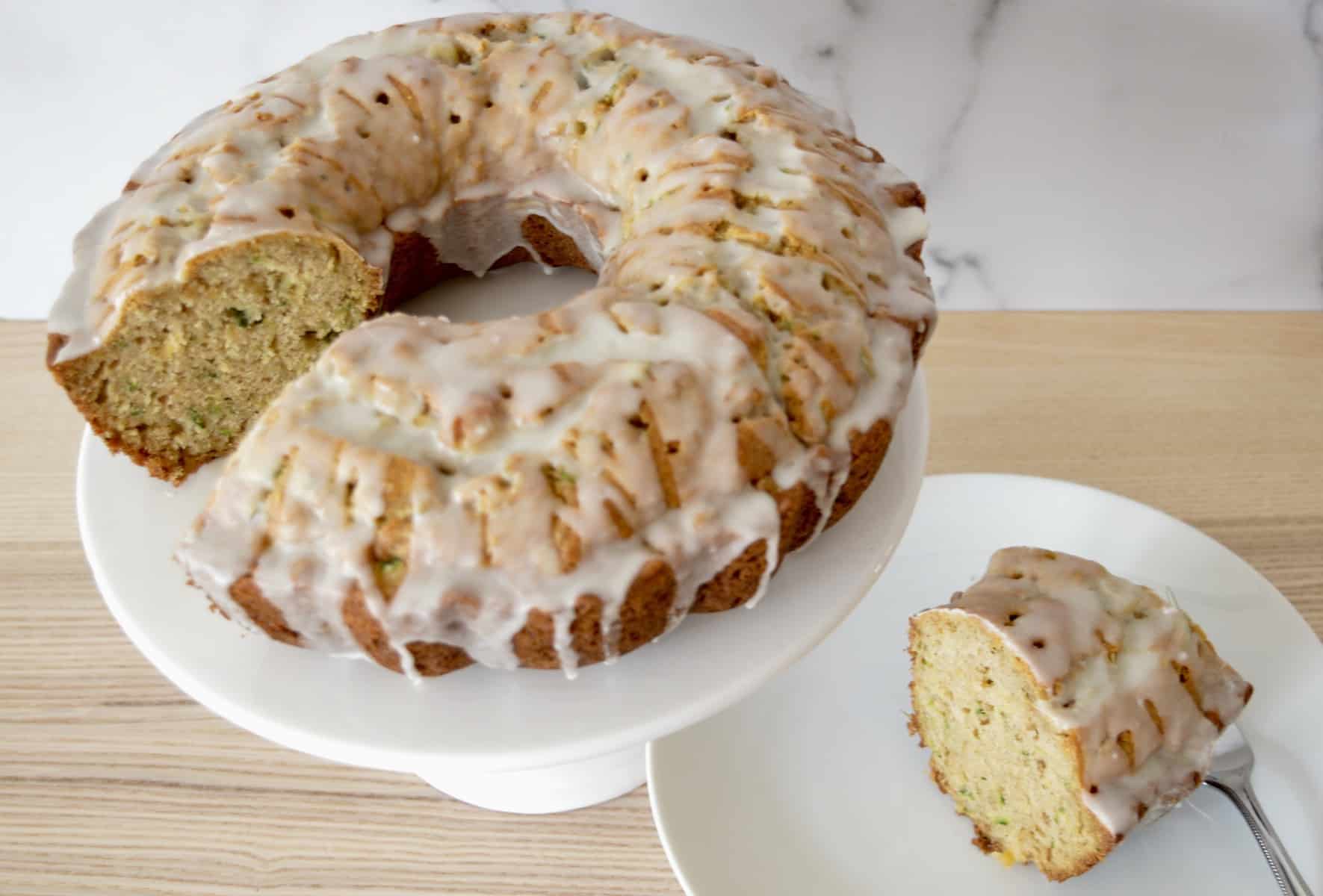 pineapple zucchini Bundt Cake on a pedestal with a slice of it in the background. 