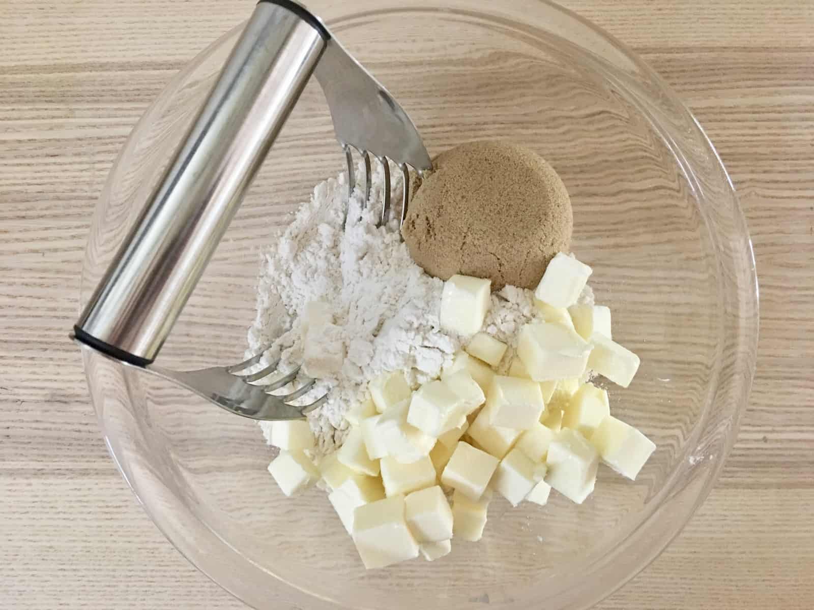 flour, butter, and brown sugar in a glass bowl with a pastry cutter. 