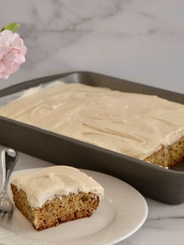 Brown butter banana cake on a white plate with carnations in the background.
