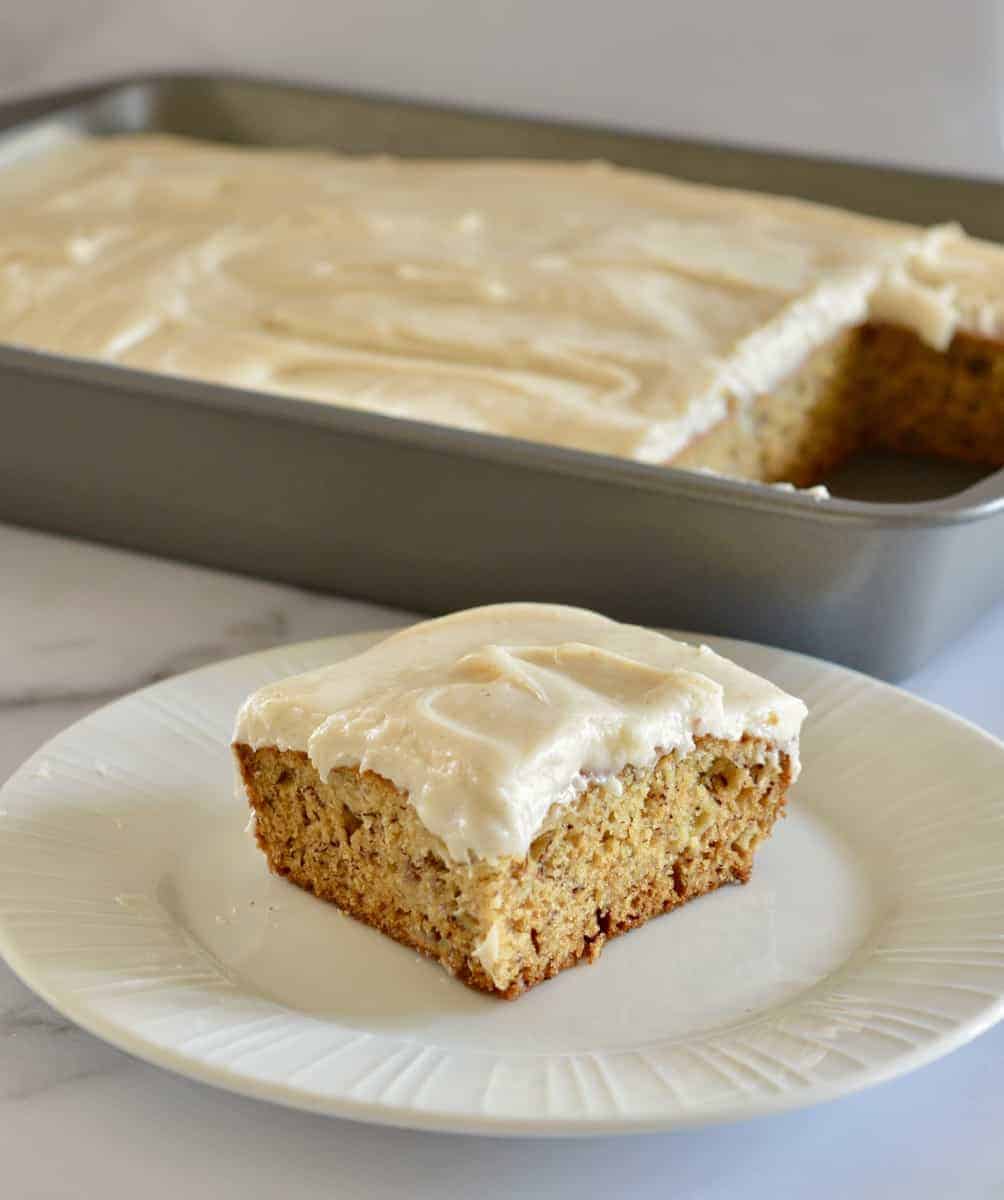 Brown butter banana cake on a plate with a tray of cake in the background.
