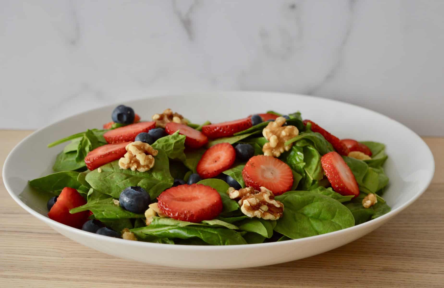 veggies and fruits in a white bowl with walnuts on top. 