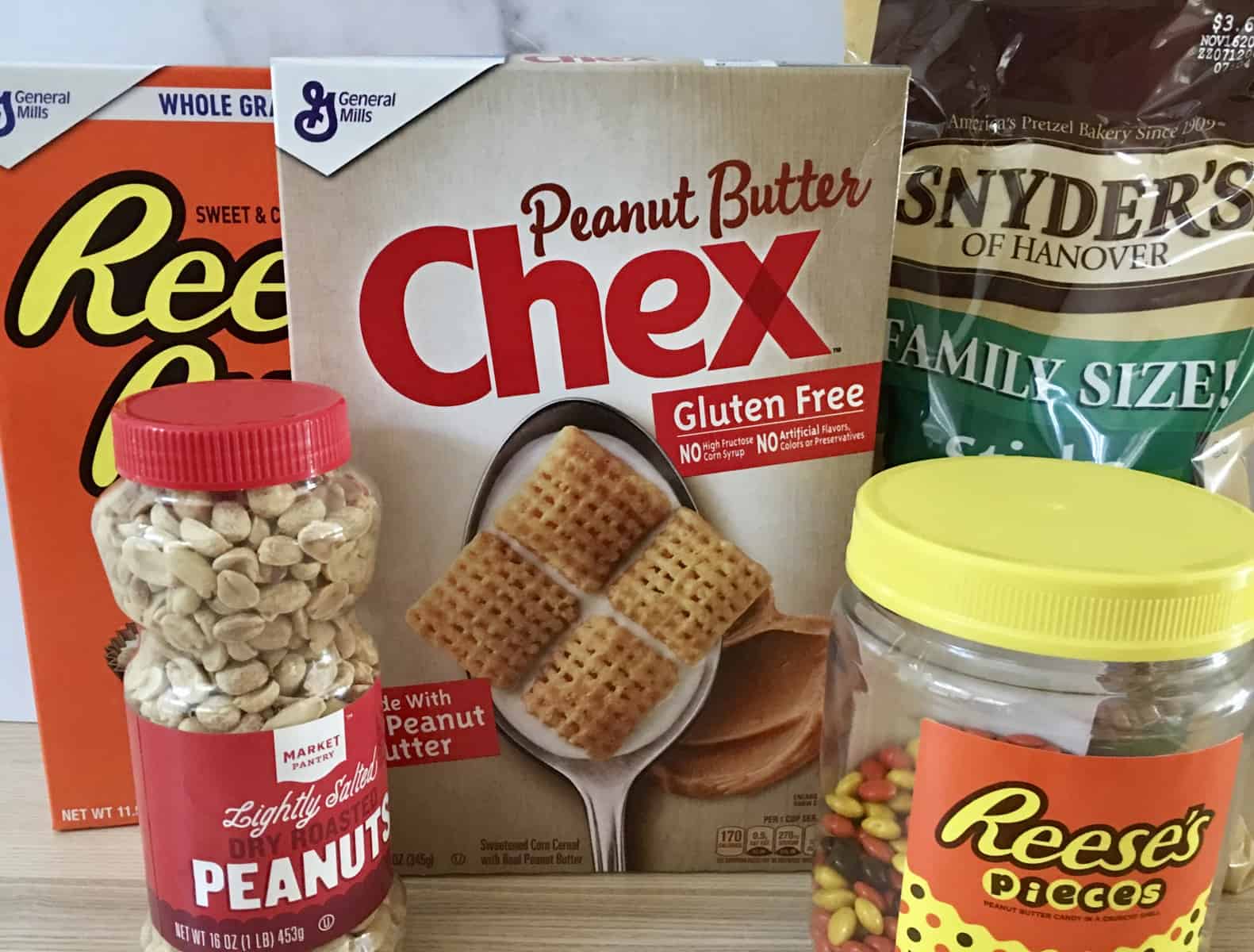 cereals, peanuts, Reese's pieces, and pretzels in their containers on a wood counter. 