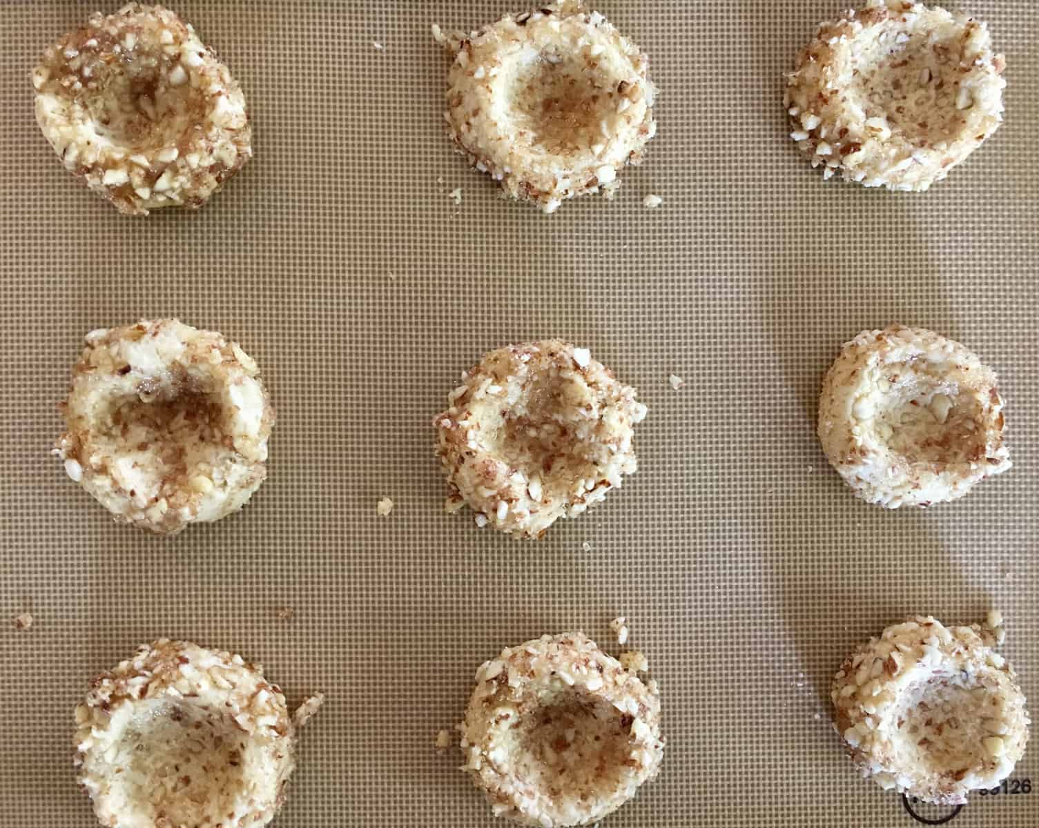 thumb indentations in the middle of cookies on a baking sheet. 