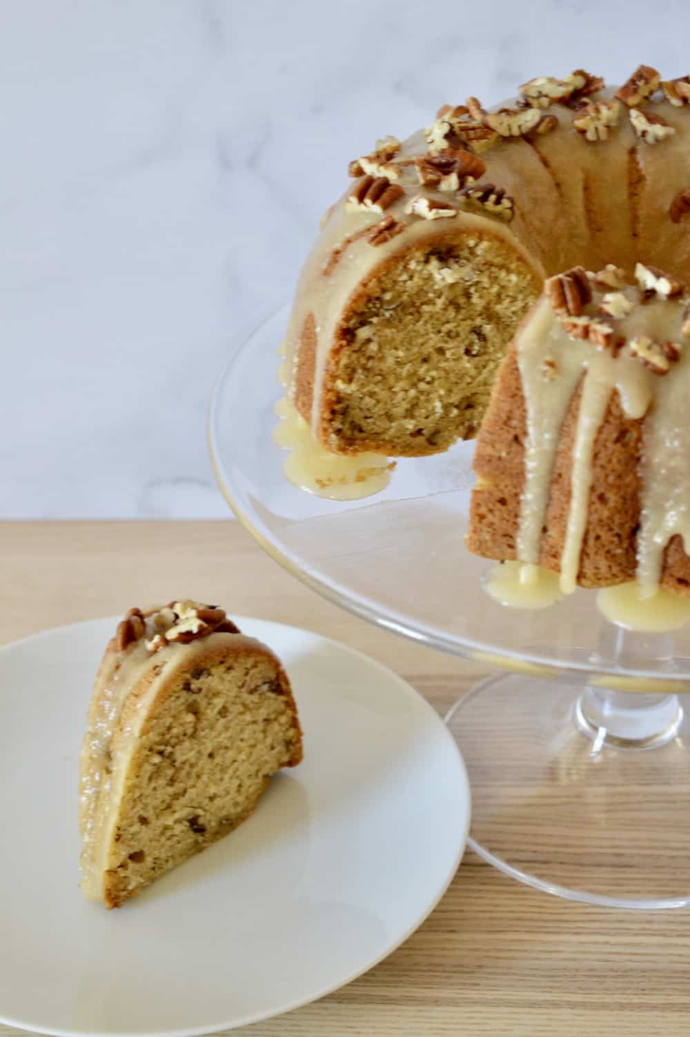 Bourbon Pecan Banana Bundt Cake with a Bourbon Butter Glaze! So moist and delicious, it's the best way to use up those ripe bananas! #bourbonpecan #bananabundtcake with bourbon butter frosting on a glass pedestal. 