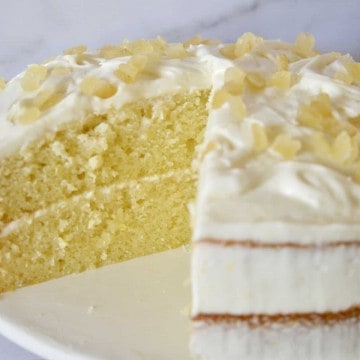 Limoncello Ricotta Cake on a white pedestal with a piece cut out of it.