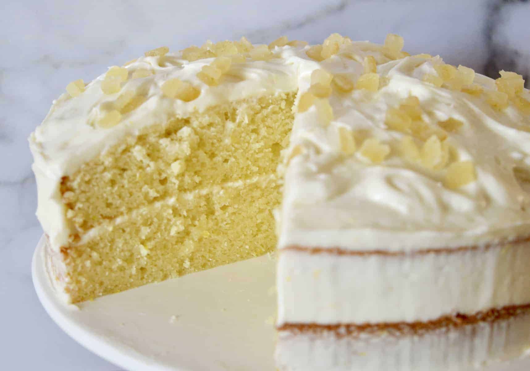 Limoncello Ricotta Cake on a white pedestal with a piece cut out of it.