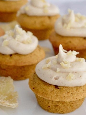 pumpkin ginger cupcakes with cream cheese frosting on a white platter with candied ginger.