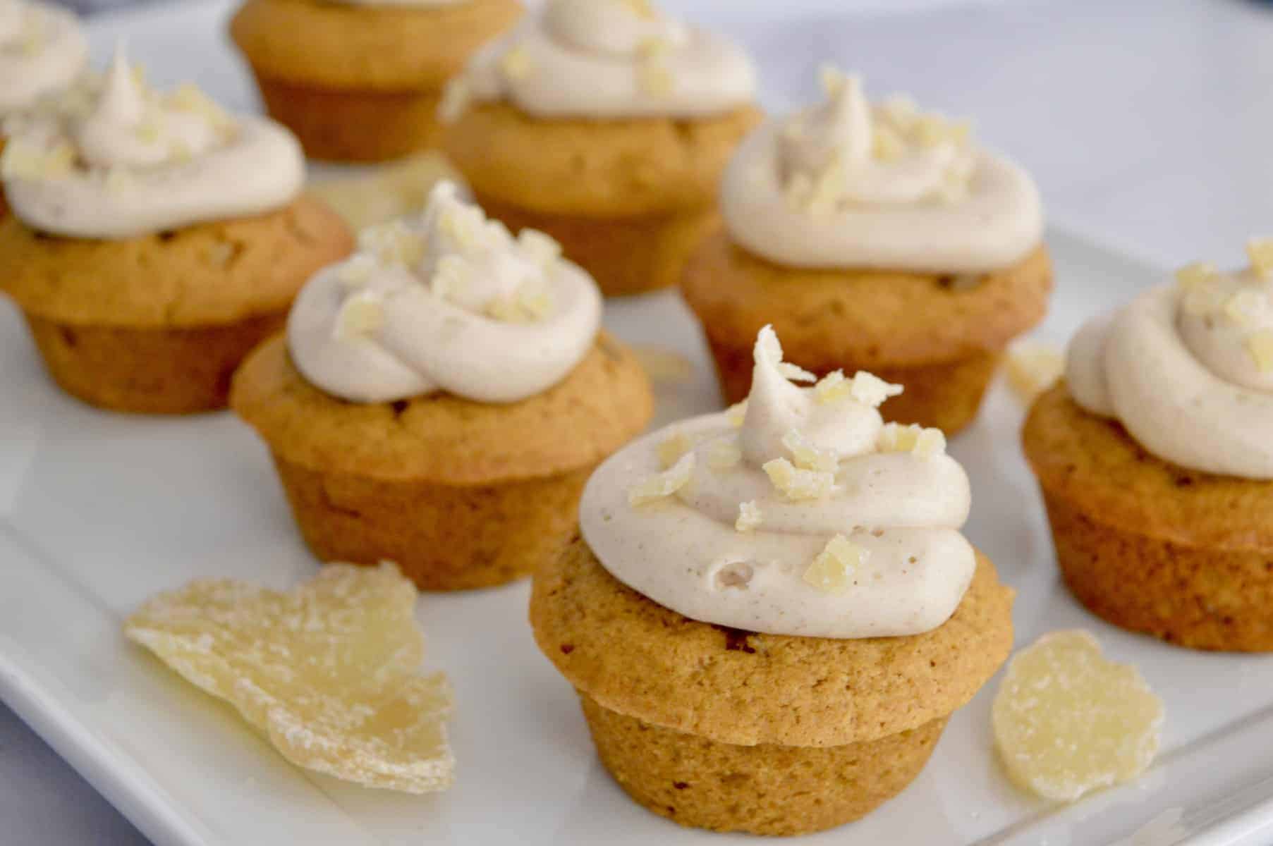 pumpkin ginger cupcakes with cream cheese frosting on a white platter with candied ginger.