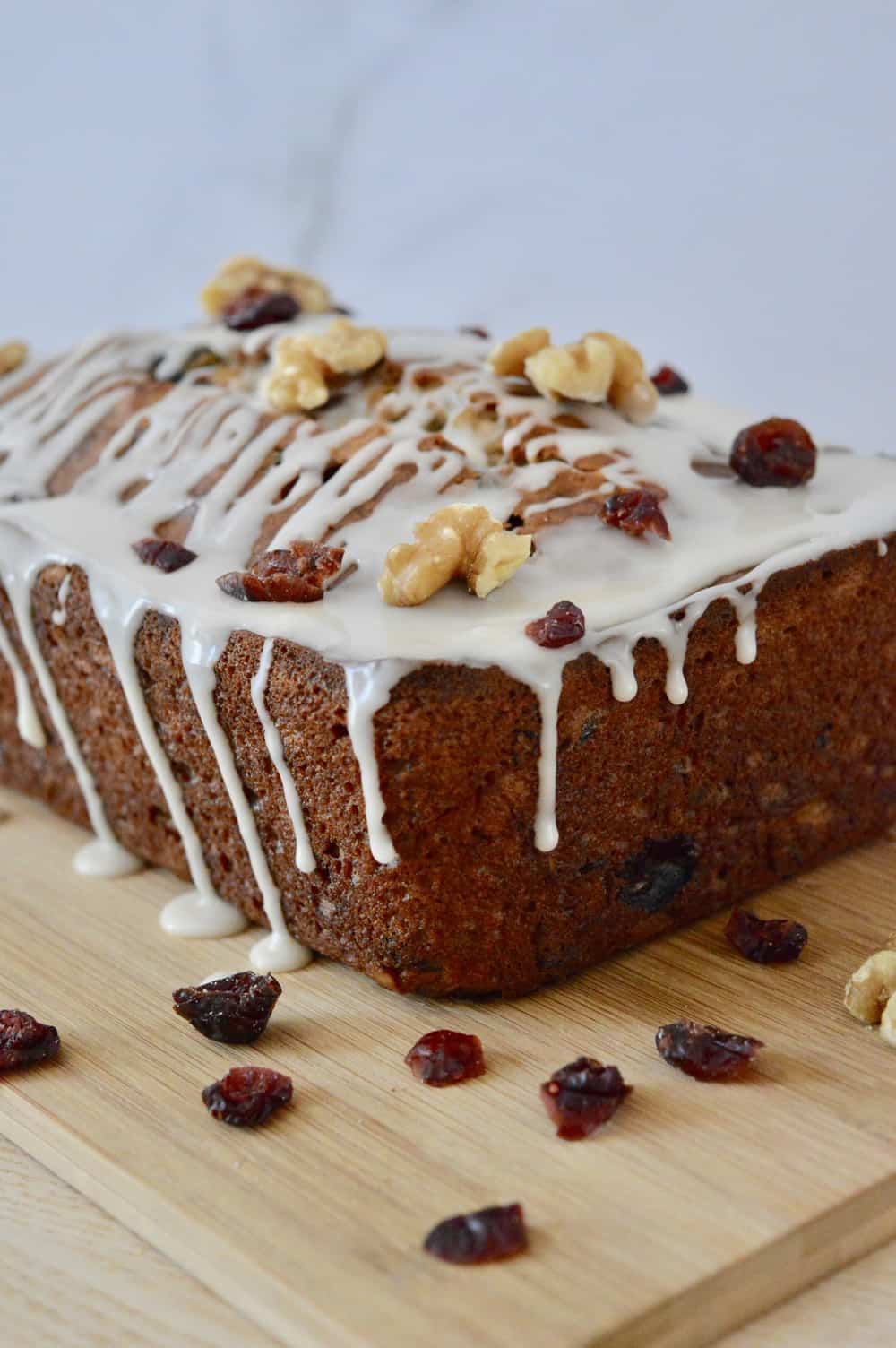 cranberry walnut banana bread with glaze dripping down it's sides on a wooden cutting board.