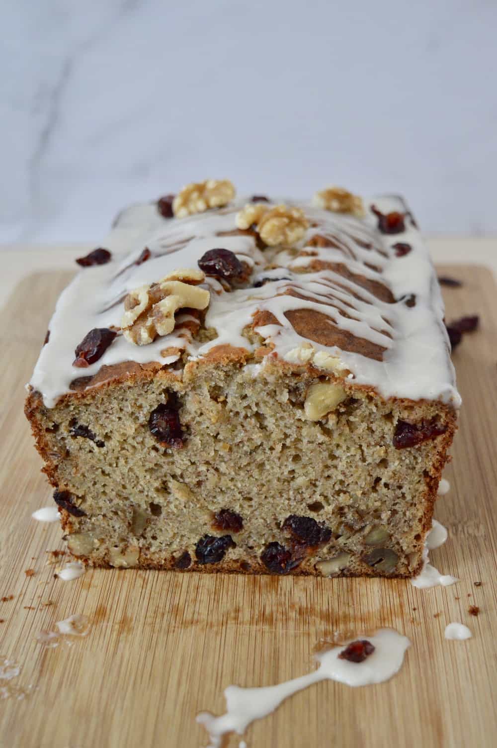 Cranberry Walnut Banana Bread with glaze on a wooden cutting board. 