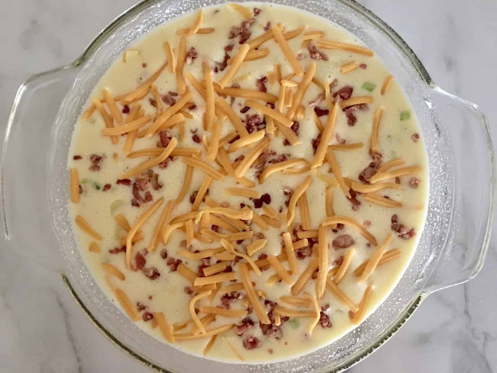 overhead photo of bacon cheddar crustless quiche ready for the oven. 