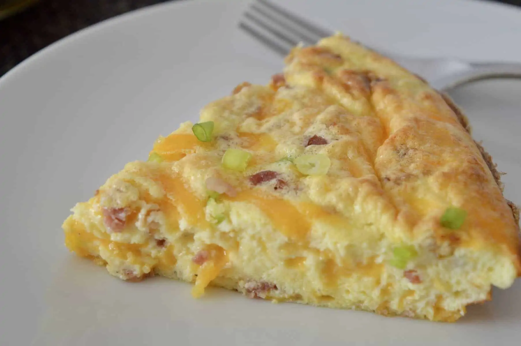 slice of crustless quiche on a white plate with a fork. 