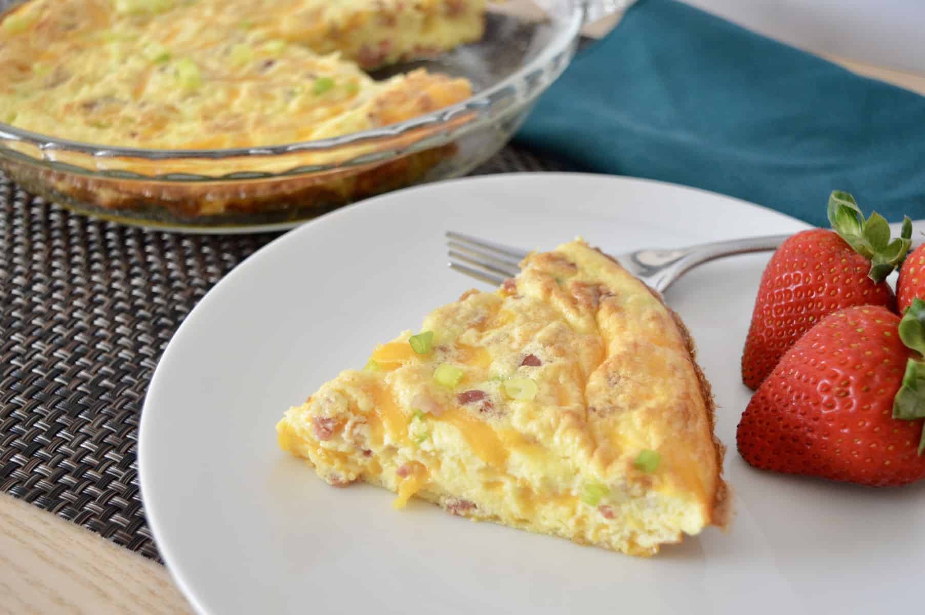 bacon and cheddar crustless quiche on a white plate with strawberries. 