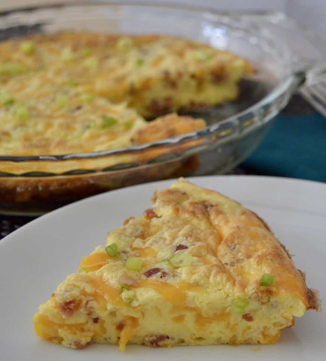 slice of quiche with glass pie pan of quiche in the background. 