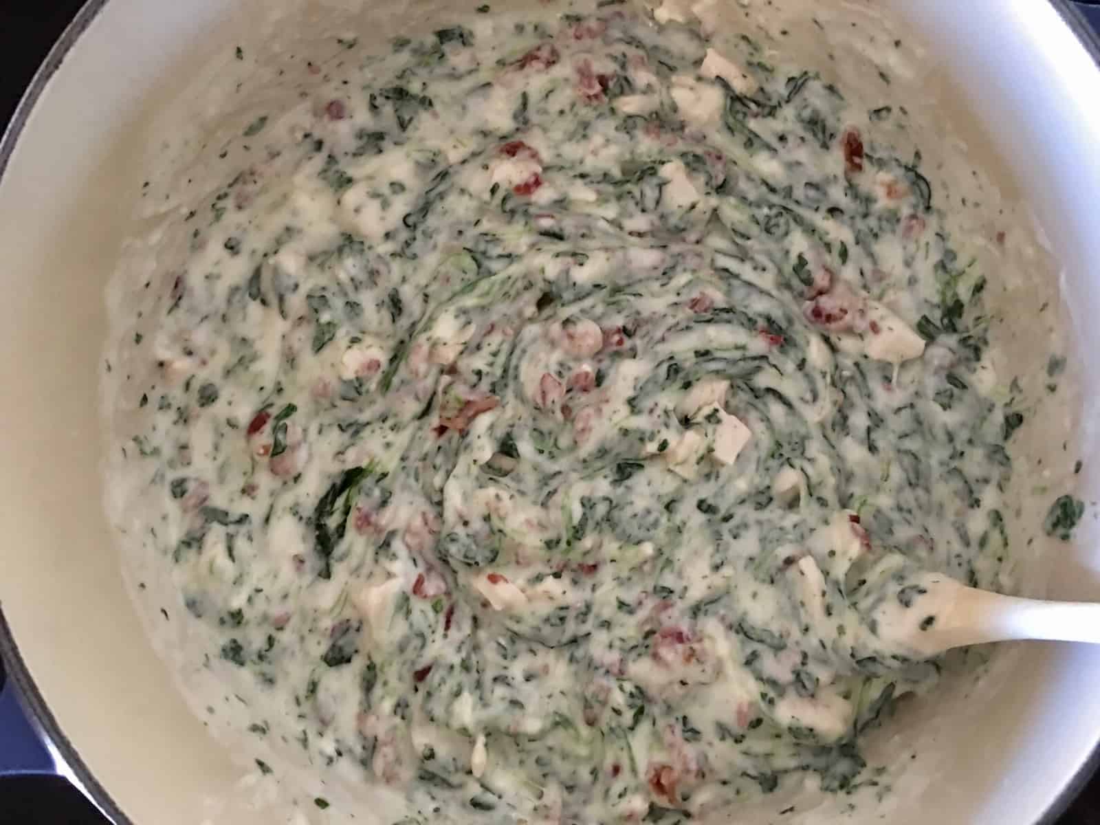 dutch oven on stove top with Alfredo sauce, spinach, bacon, and chicken stirred in. 