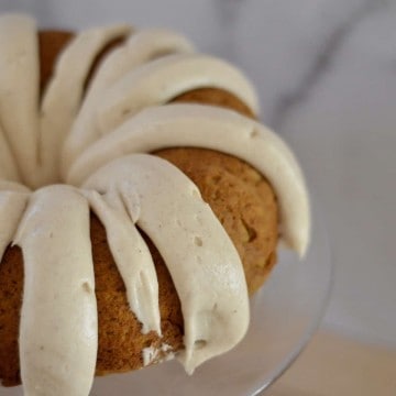 pumpkin spice bundt cake with cream cheese frosting on a glass pedestal.