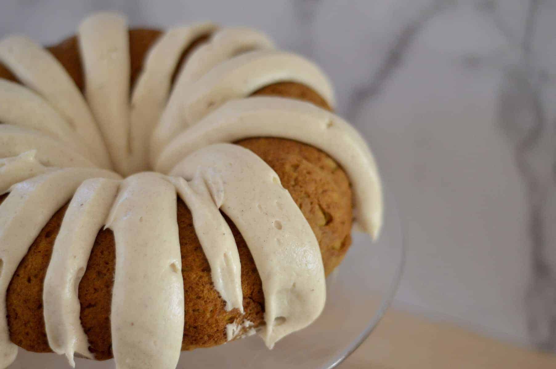pumpkin spice bundt cake with cream cheese frosting on a glass pedestal. 