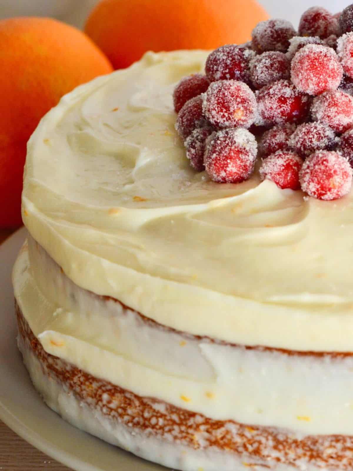 Cranberry orange cake layered with sugared cranberries on top and an orange cream cheese frosting. 