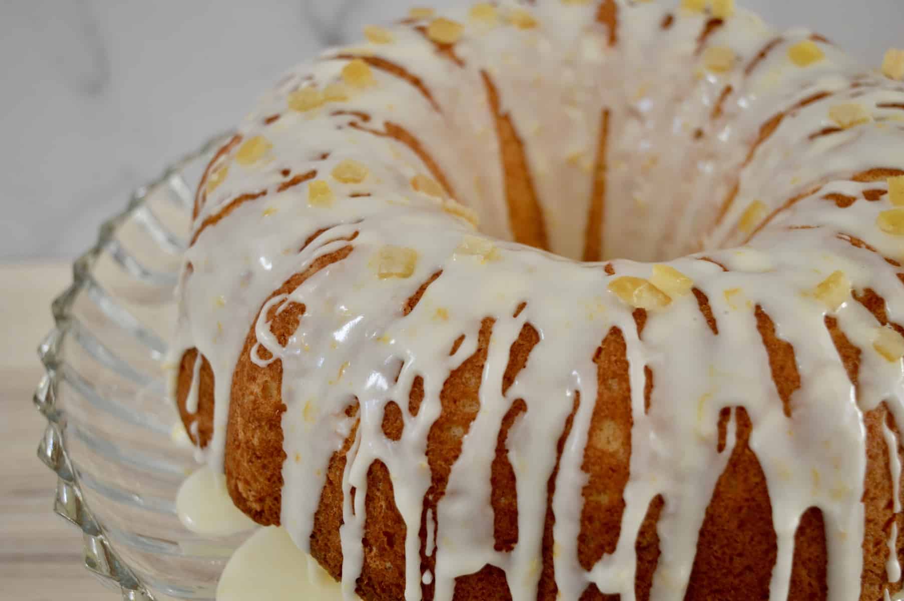 Italian bundt cake on a glass pedestal with drizzle and candied citrus peel on it. 