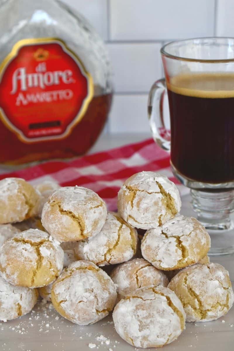 cookies piled high on a counter with a bottle of amaretto and a cup of coffee behind them. 