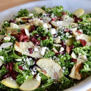 Kale Cranberry Feta Salad with almonds and apples in a white serving platter.