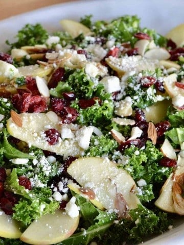 Kale Cranberry Feta Salad with almonds and apples in a white serving platter.