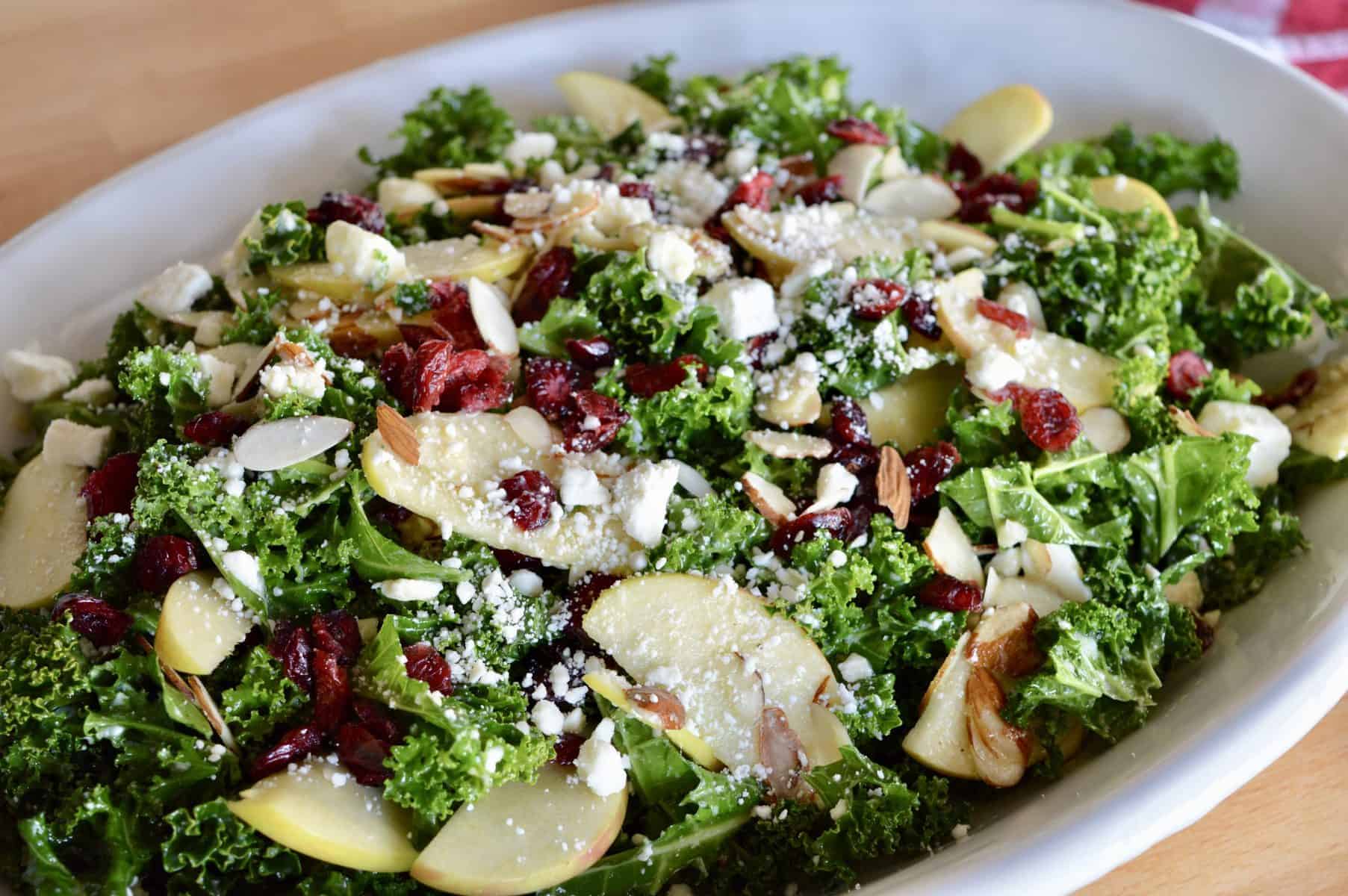 Kale Cranberry Feta Salad with almonds and apples in a white serving platter. 