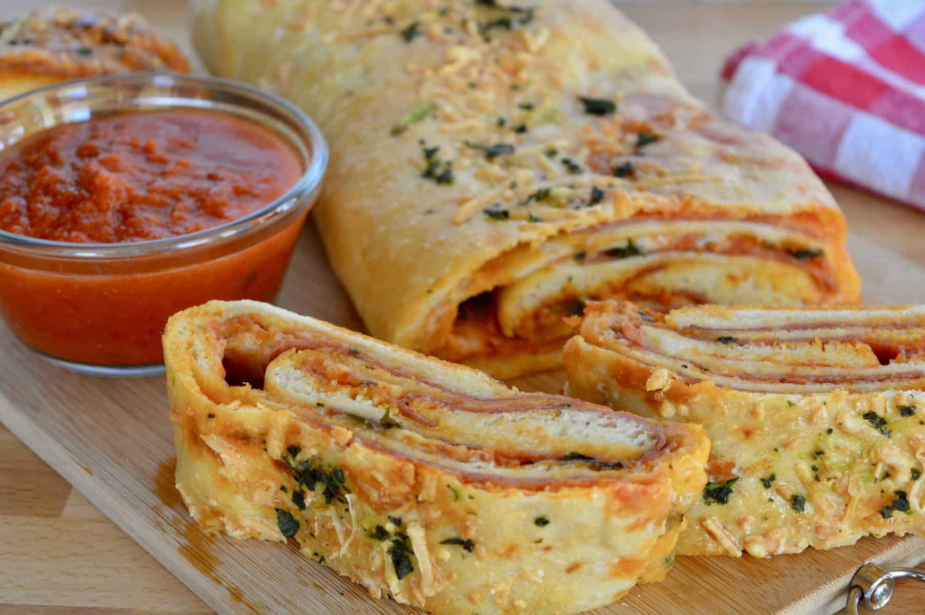 Italian Stromboli Recipe on a cutting board with marinara sauce for dipping. 